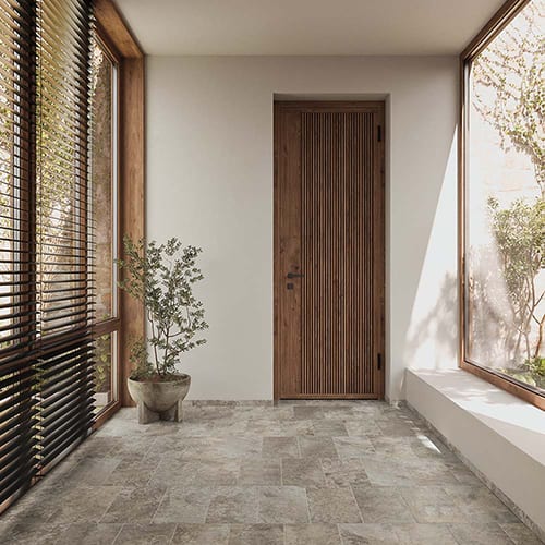 A minimalist hallway with a wooden slatted door, large windows with blinds, a potted plant, and a tiled floor.