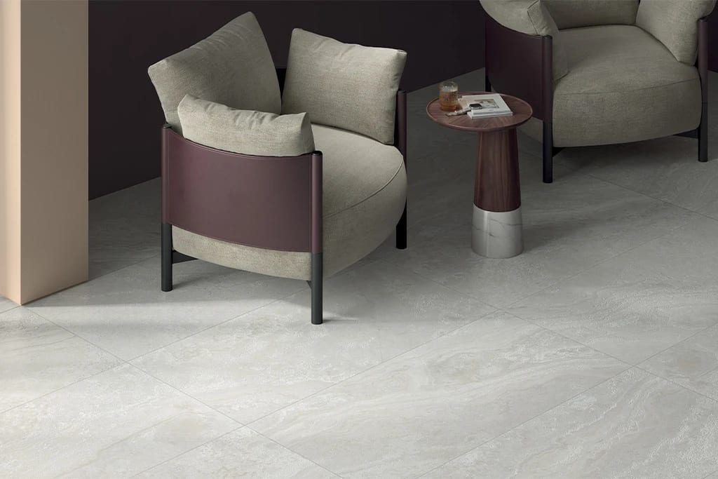 Two modern armchairs, a side table, and light-colored patterned floor tiles in a dimly lit room.