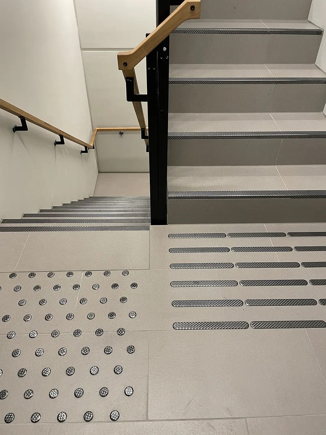 Staircase with wooden handrails, anti-slip strips, and tactile paving: studs and direction bars.