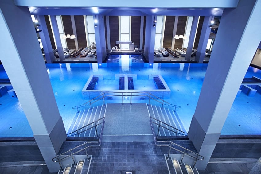 A modern indoor pool with vivid blue water, elegant architecture, and lounge seating.