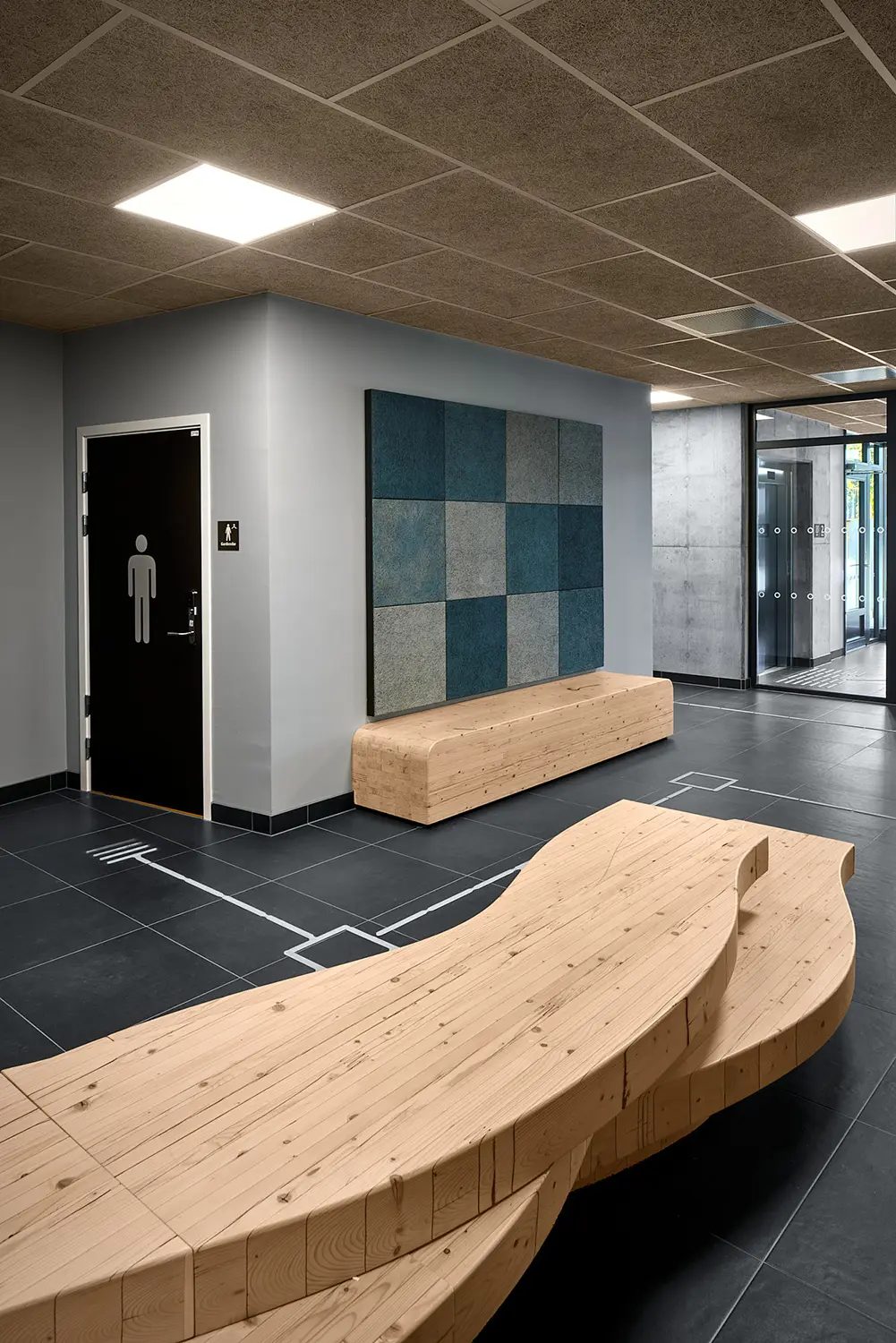 Modern hallway with curved wooden benches, checkered acoustic wall panel, and dark tiled floor.
