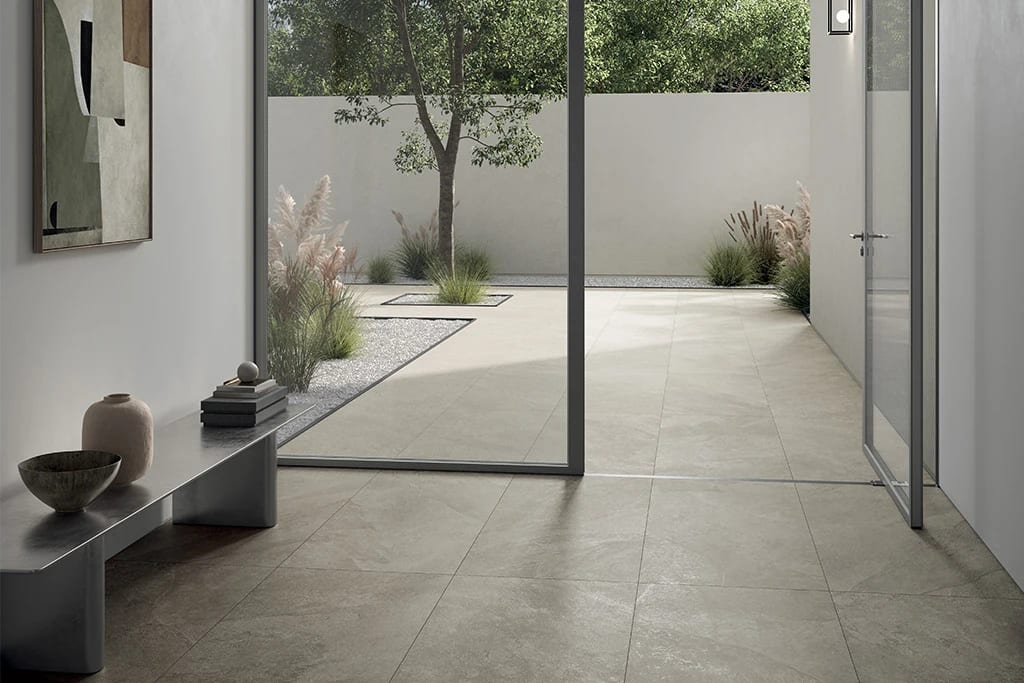 Modern tiled interior opens via glass doors to a patio with a tree and pampas grass.