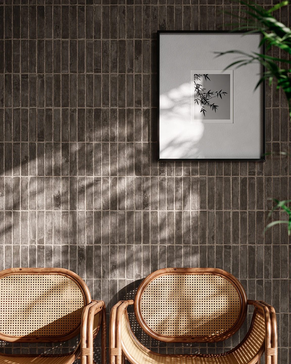 Dark tiled wall, framed bamboo print, two rattan chairs, and plant shadows.