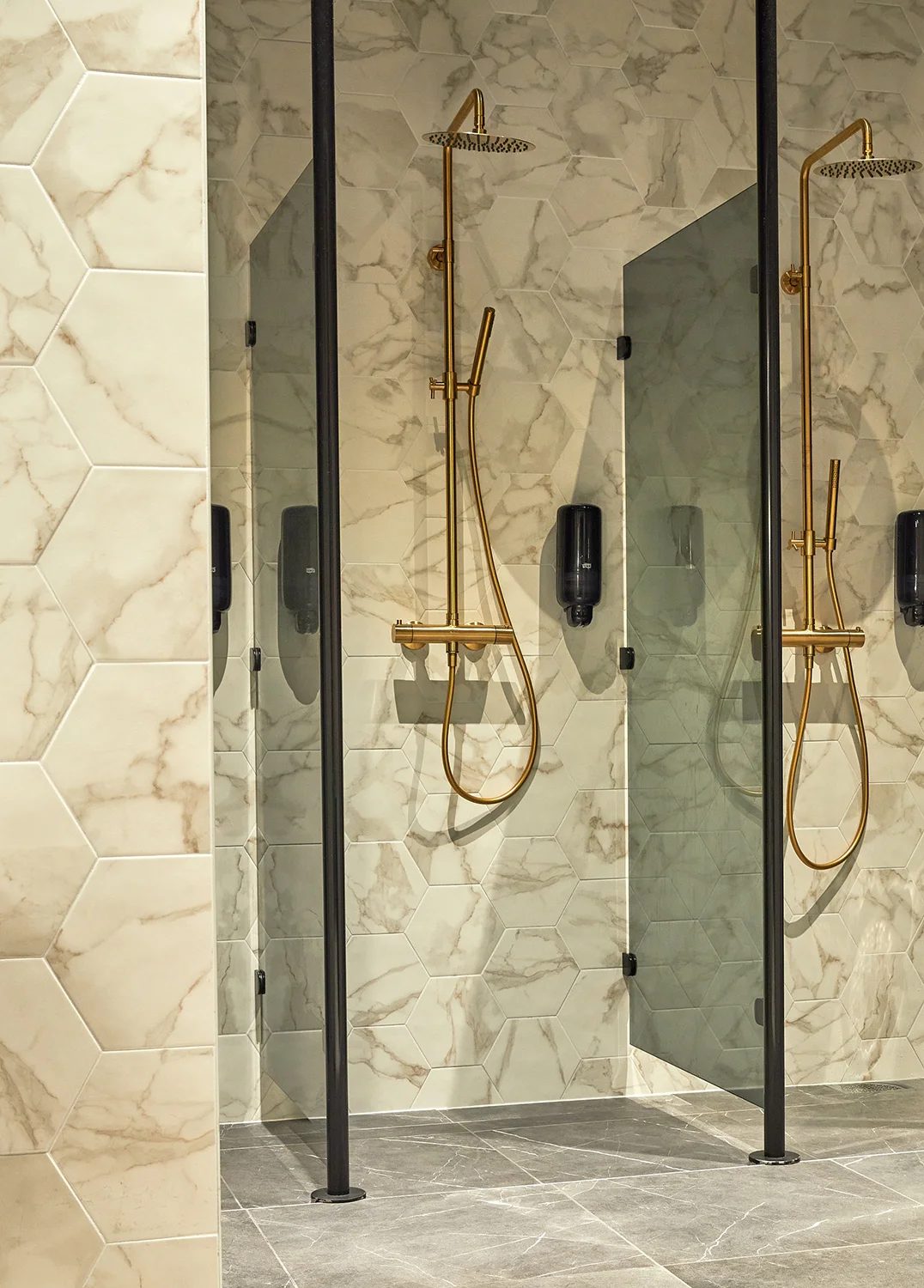 Modern showers with gold fixtures, hexagonal marble tiles, and gray floor.