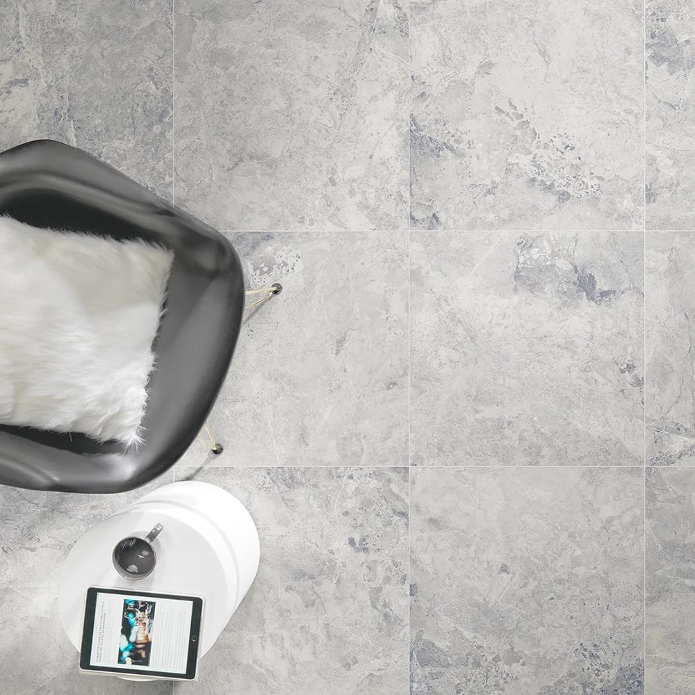 Overhead of light gray marble-look tiled floor, chair with white pillow, and table with tablet.