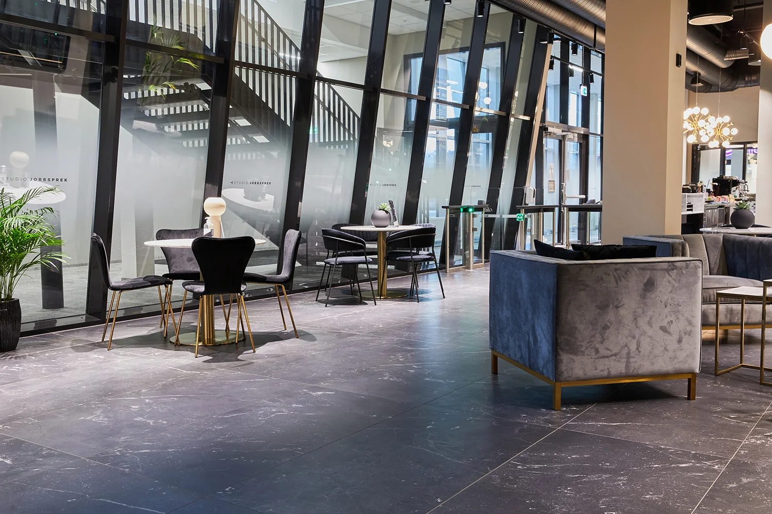 Modern lounge with dark marble floor, velvet seating, tables, and large glass partitions.
