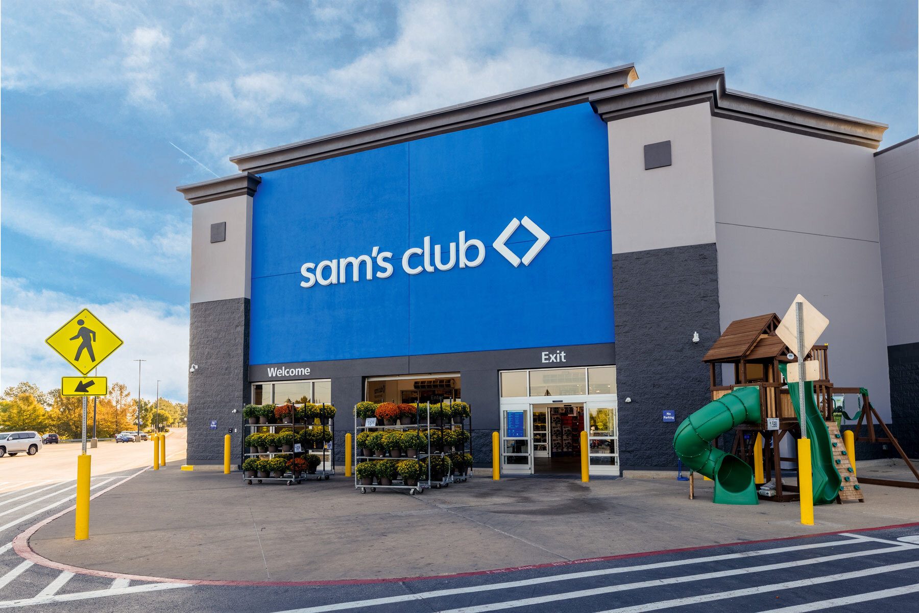Sam's Club store exterior with a blue logo wall, entrance, flower displays, and a playground.