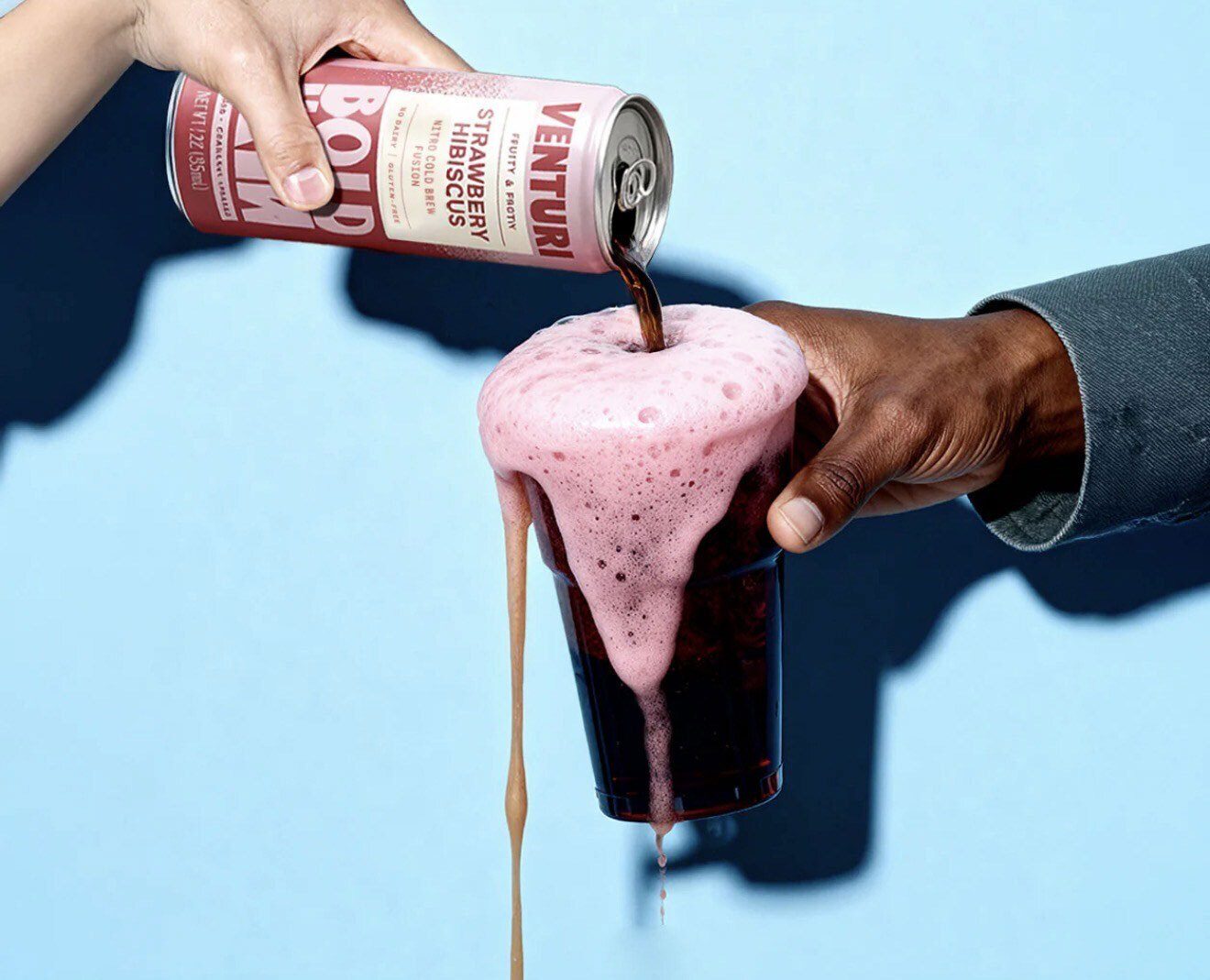 A can of Venturi Strawberry Hibiscus Nitro Cold Brew is poured into a glass, overflowing with pink foam.