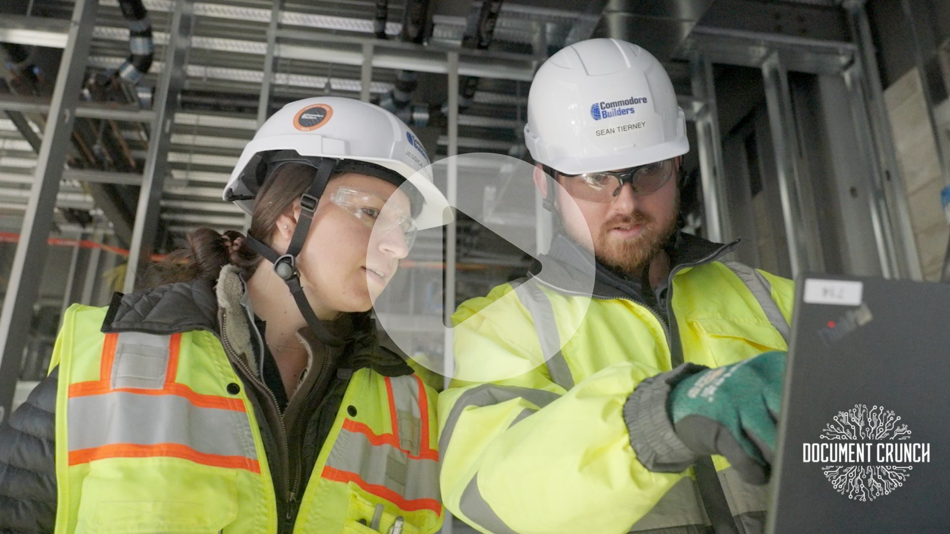 Video thumbnail: Two construction workers in hard hats and safety gear review a laptop at a construction site.