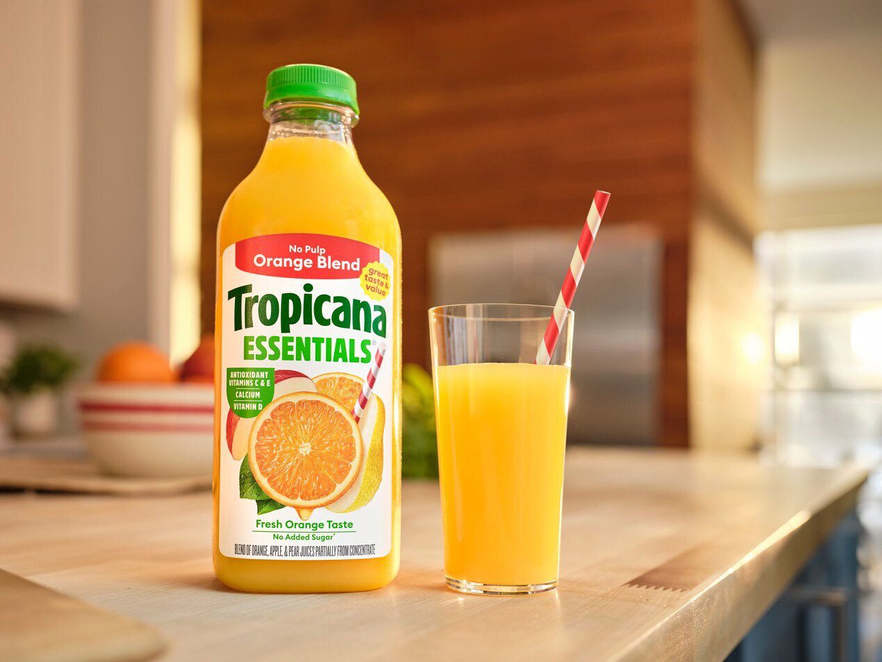 Tropicana Essentials Orange Blend juice bottle and a glass with a red and white straw.