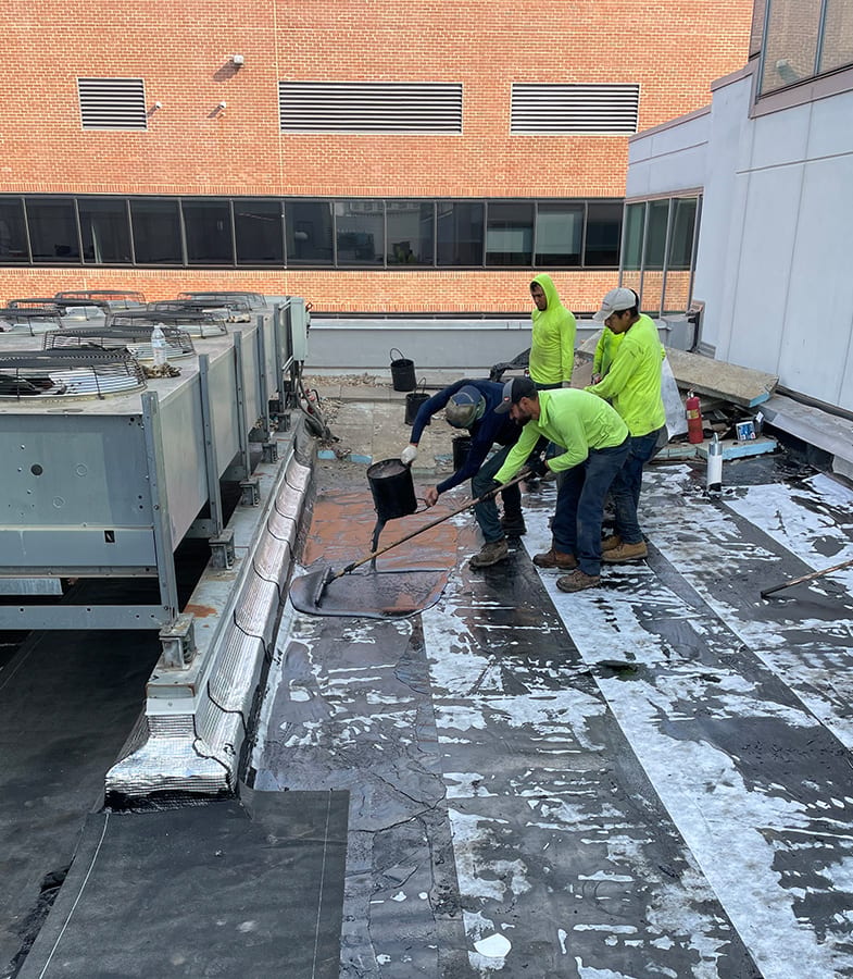 Crew hot applying rubberized asphalt to a commercial roof.