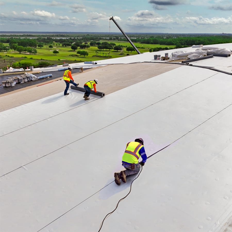 Three roofers in safety gear atop the Savannah Convention Center installing PVC membrane.