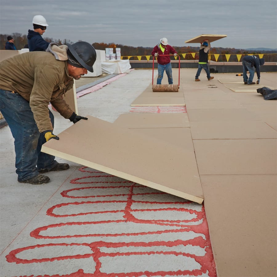 Roofing crew adhering sections of coverboard to a commercial roof.