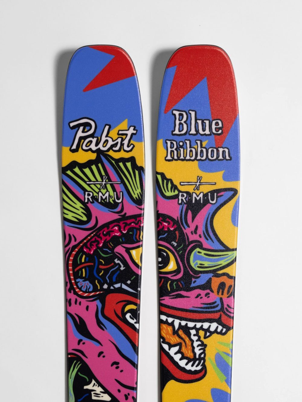 Two vibrant Pabst Blue Ribbon x RMU skis featuring bold, colorful dragon artwork.
