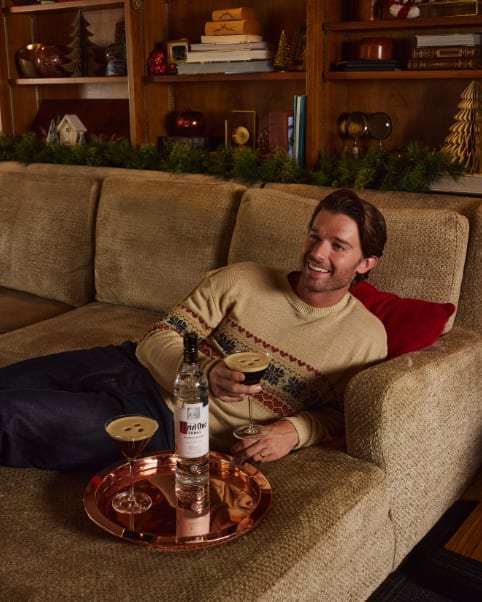 Smiling man on a couch with two dark martinis and Ketel One vodka on a copper tray.