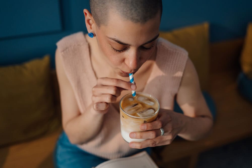 Person with short hair drinking iced coffee with a blue and white striped straw.