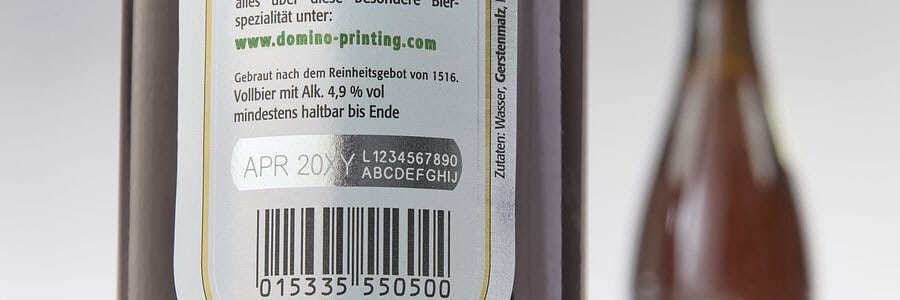 Beer bottle label with "APR 20XY" best-by date, batch, barcode, German text, and domino-printing.com.