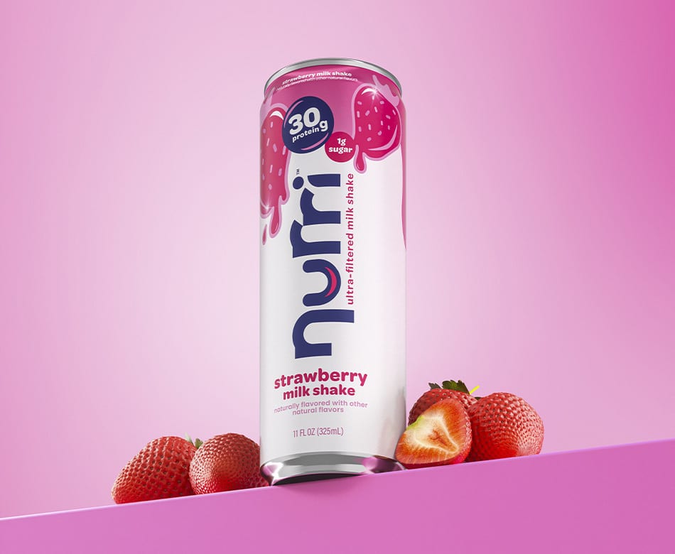 Nurri strawberry milk shake can (30g protein, 1g sugar) with fresh strawberries on pink.