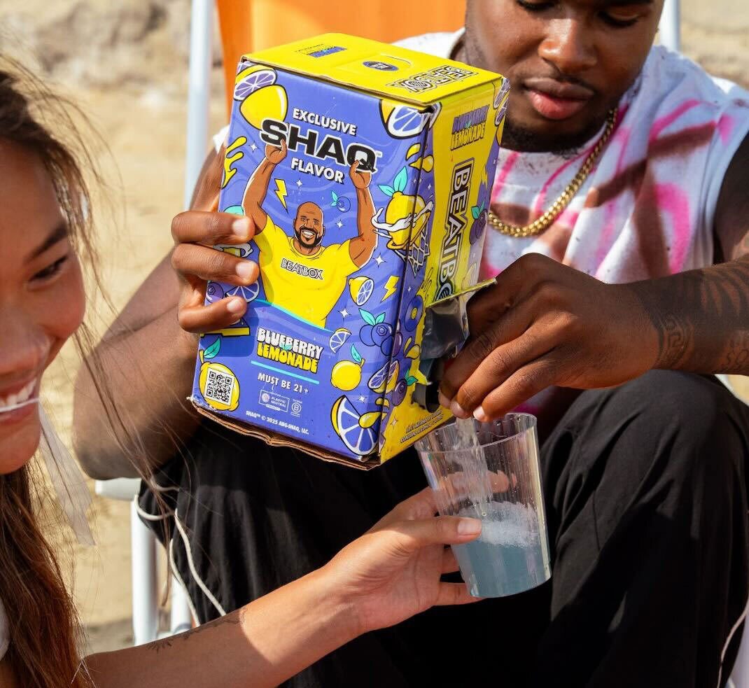 Man pours blue "Shaq Flavor BeatBox Blueberry Lemonade" from a box into a woman's cup.