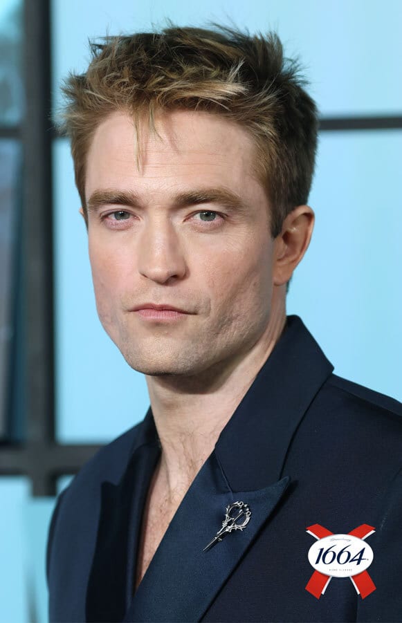 Close-up of Robert Pattinson with a serious expression, wearing a dark suit and a decorative pin.