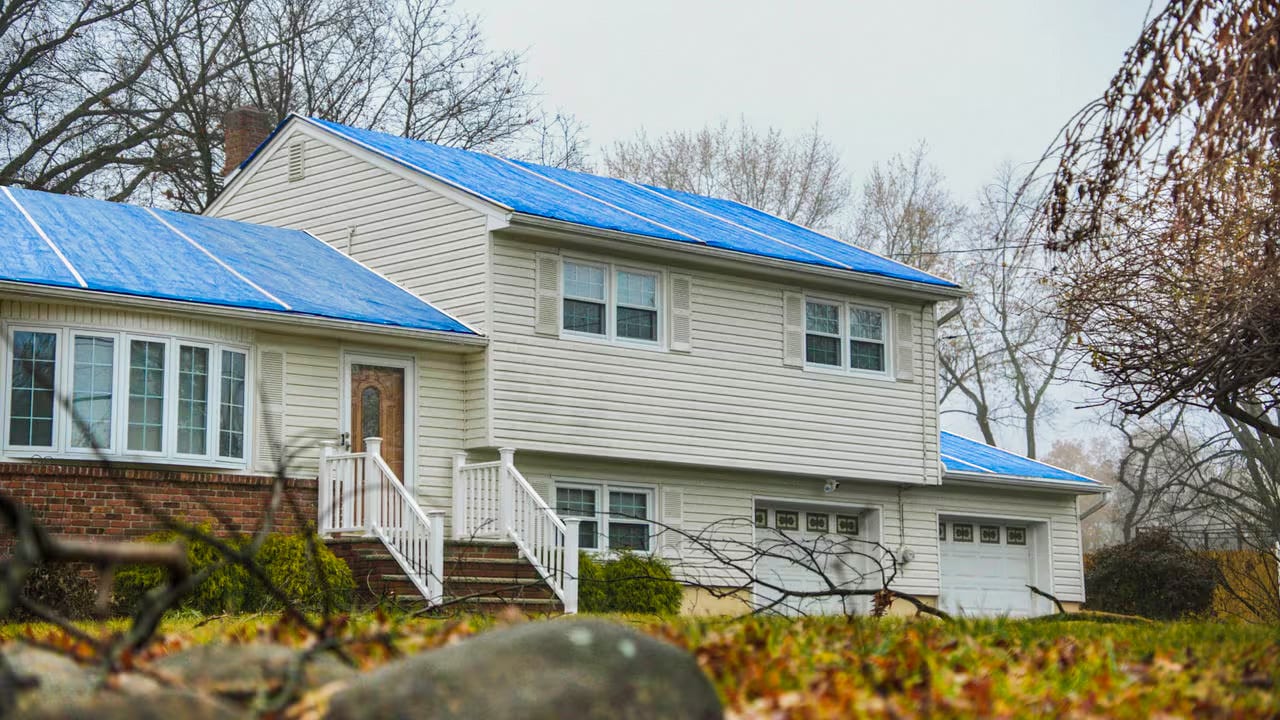 Residential home roof covered in blue protective covering.