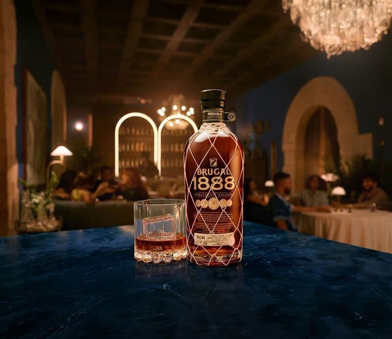 Brugal 1888 rum bottle and glass on a dark blue counter in a dimly lit bar scene.