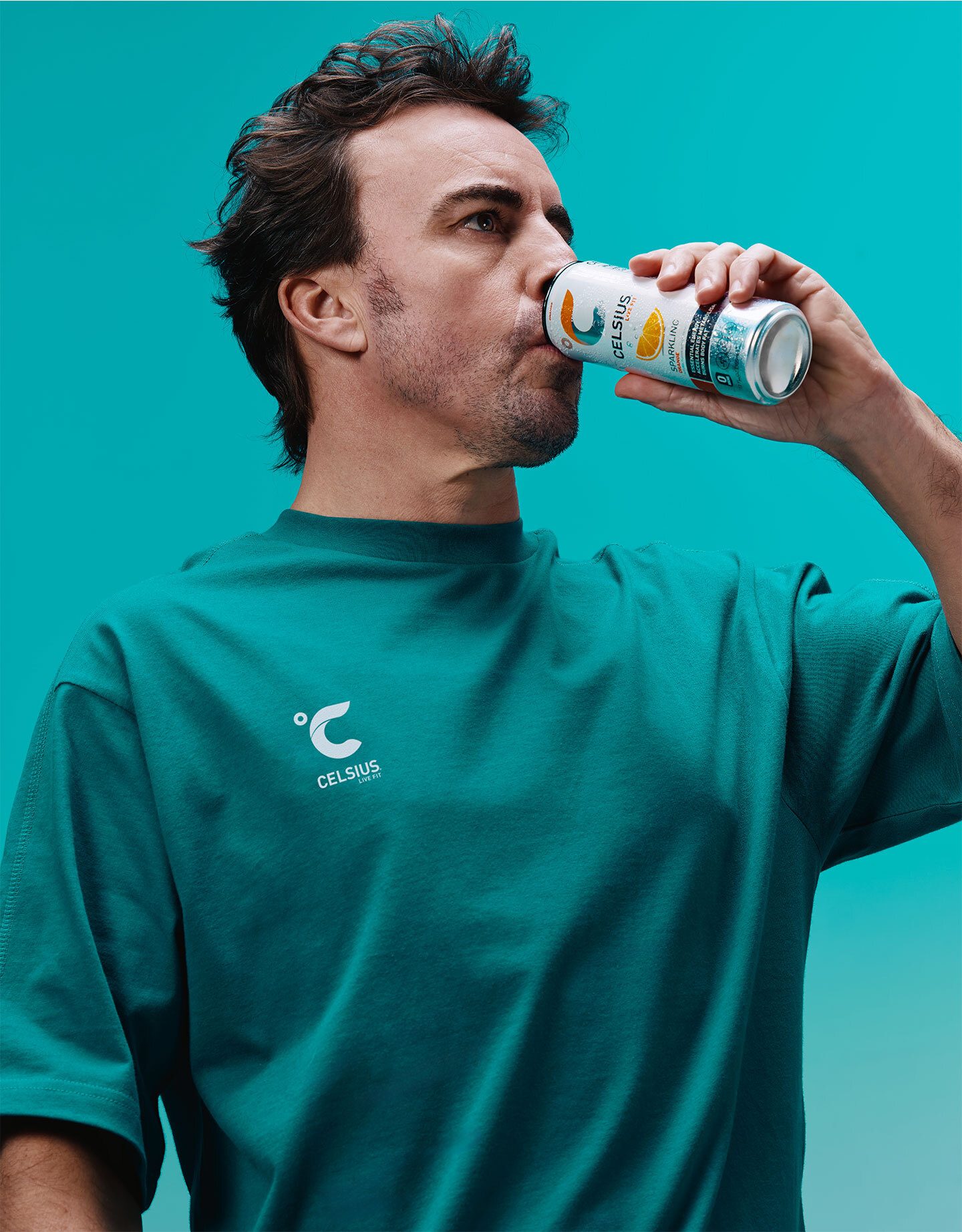 Man in teal shirt drinking Celsius energy drink from a can.