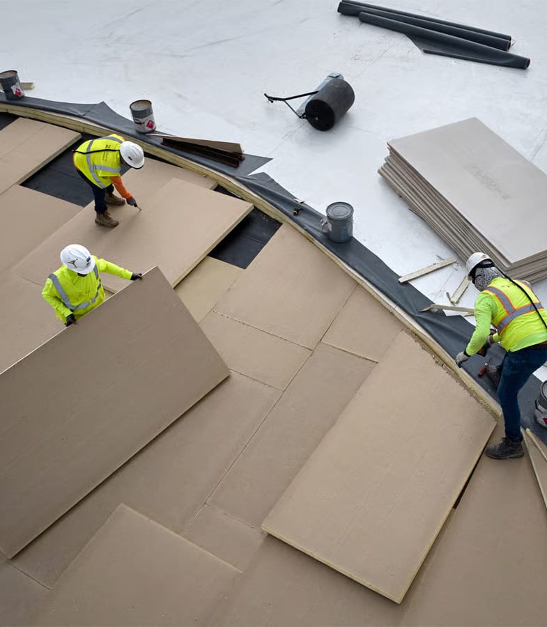 Overhead view of three roofers in safety gear placing large sections on coverboard.