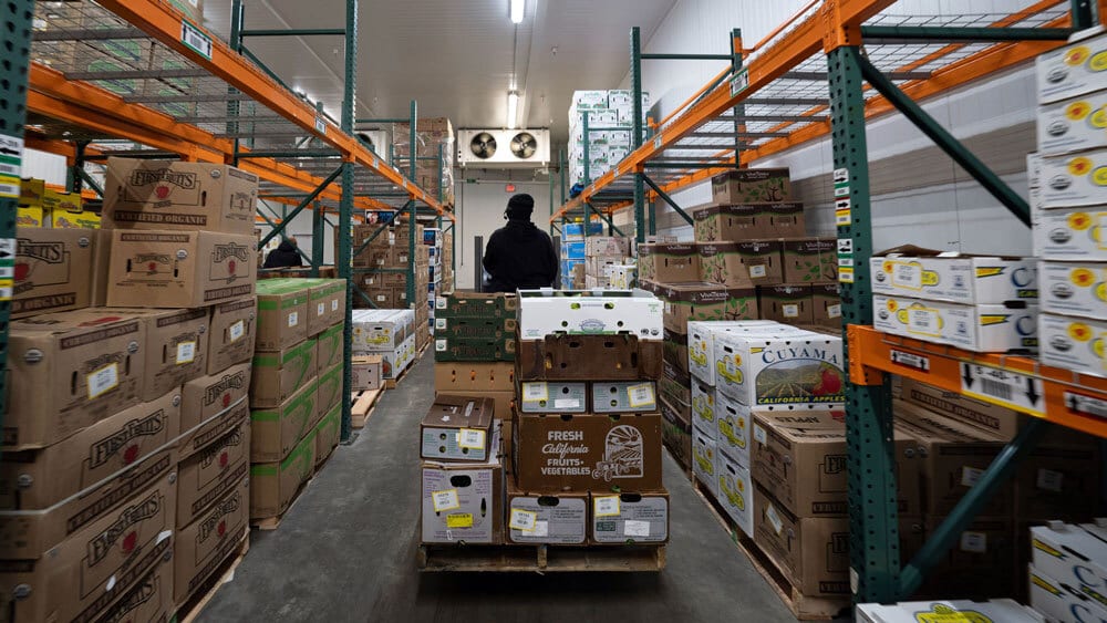A person pushes a pallet of boxes in a cold storage warehouse aisle.