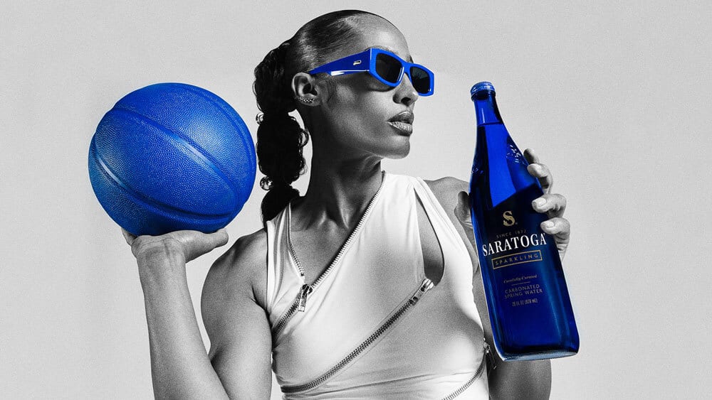 Woman in B&W with blue basketball, Saratoga sparkling water bottle, and blue sunglasses.