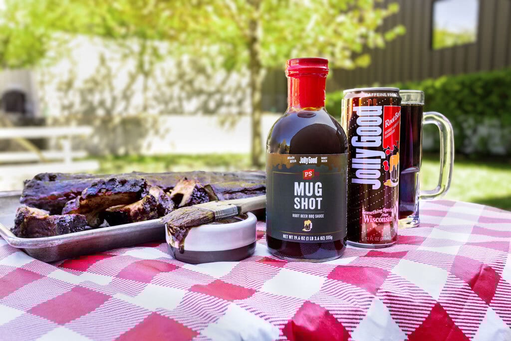BBQ ribs, root beer sauce, and drink on a red checkered picnic table outdoors.