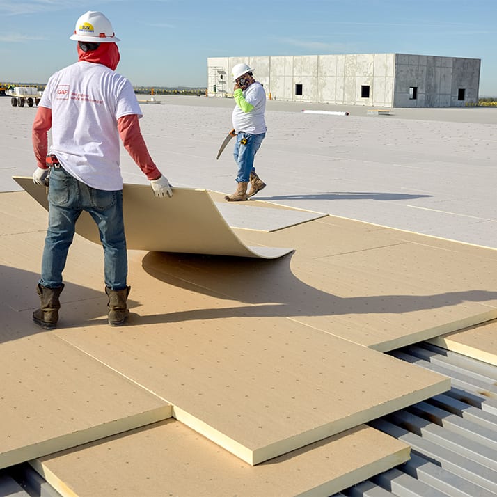 Two roofers in hard hats laying out sections of insulation.