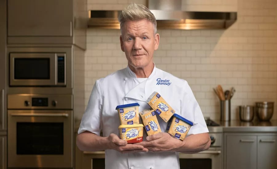 Gordon Ramsay in a kitchen, holding multiple tubs of I Can't Believe It's Not Butter!