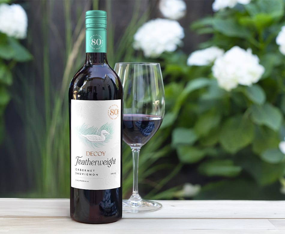 Decoy Featherweight 80-calorie wine bottle and glass of red wine in a garden setting.