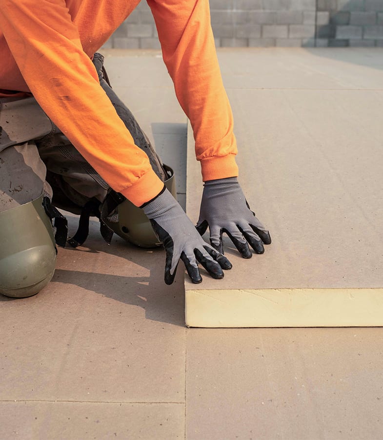 Closeup of a roofers gloved hands on the corner of a thick section of insulation.