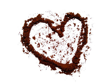Heart shape drawn with dark brown coffee grounds on a clean white background, viewed from above.