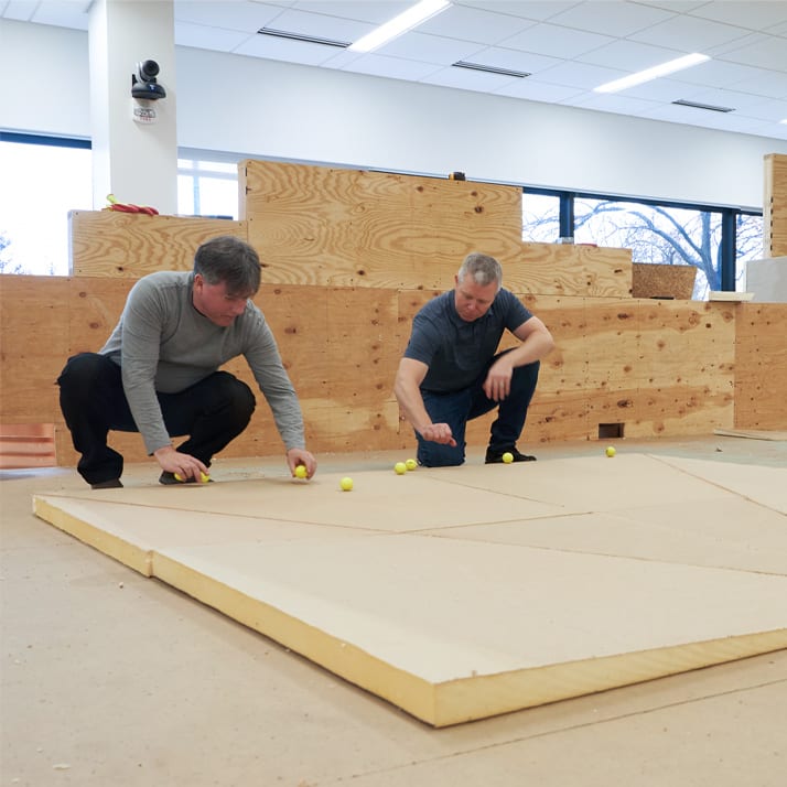 Two engineered demonstrating tapered insulation by rolling yellow balls over the surface in a test setting.