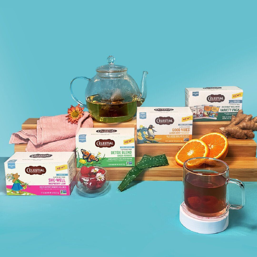An assortment of Celestial Seasonings wellness teas, a teapot, and mug with fresh ingredients like oranges and ginger.