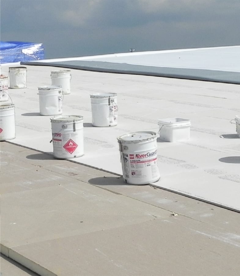 Multiple white buckets weighing down newly installed polyiso insulation.