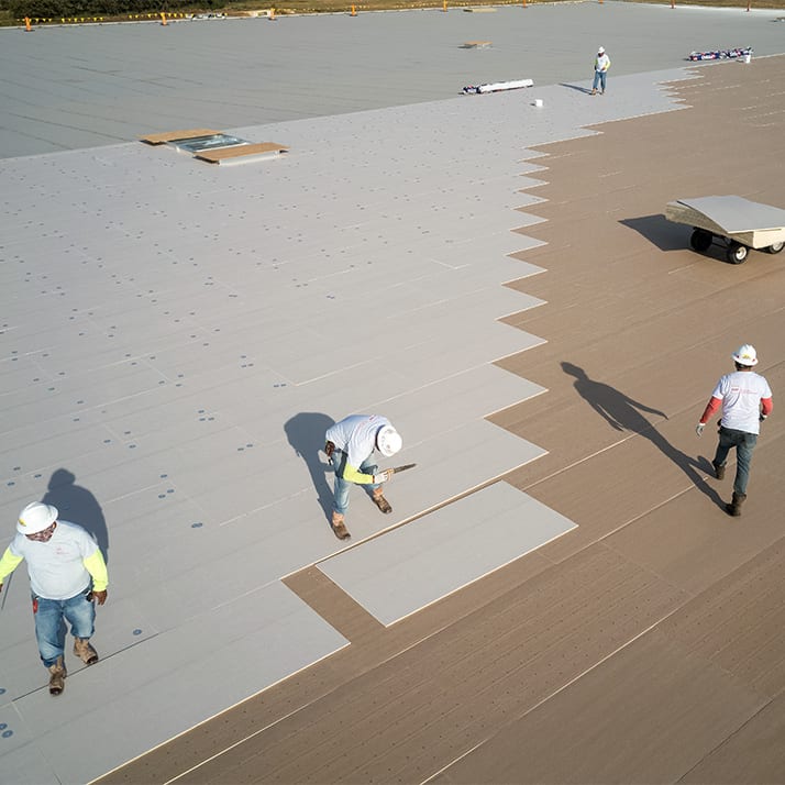 Overhead view of roofing crew in hard hats laying down coverboard.