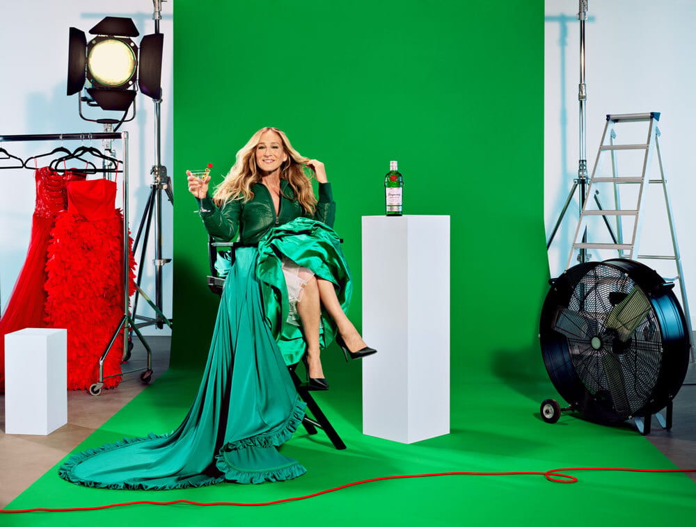 Sarah Jessica Parker in a green dress, holding a martini, against a green screen.