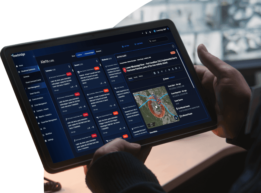 Person holding a tablet displaying an Everbridge alert dashboard with critical event details and a map.