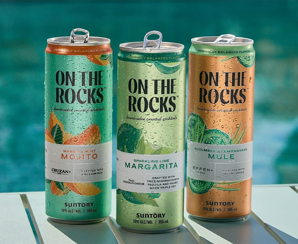 Three colorful On The Rocks canned cocktails (Mojito, Margarita, Mule) by a pool.