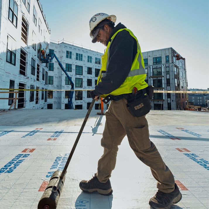 Roofer smoothing vapor retarder with a roller.