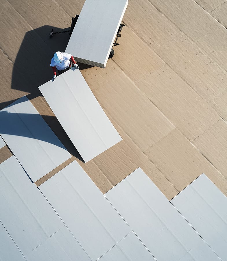 Overhead view of a roofter in hard hat placing sections of coverboard.