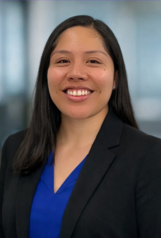 Professional headshot of a smiling woman with dark hair wearing a black blazer and a blue top.