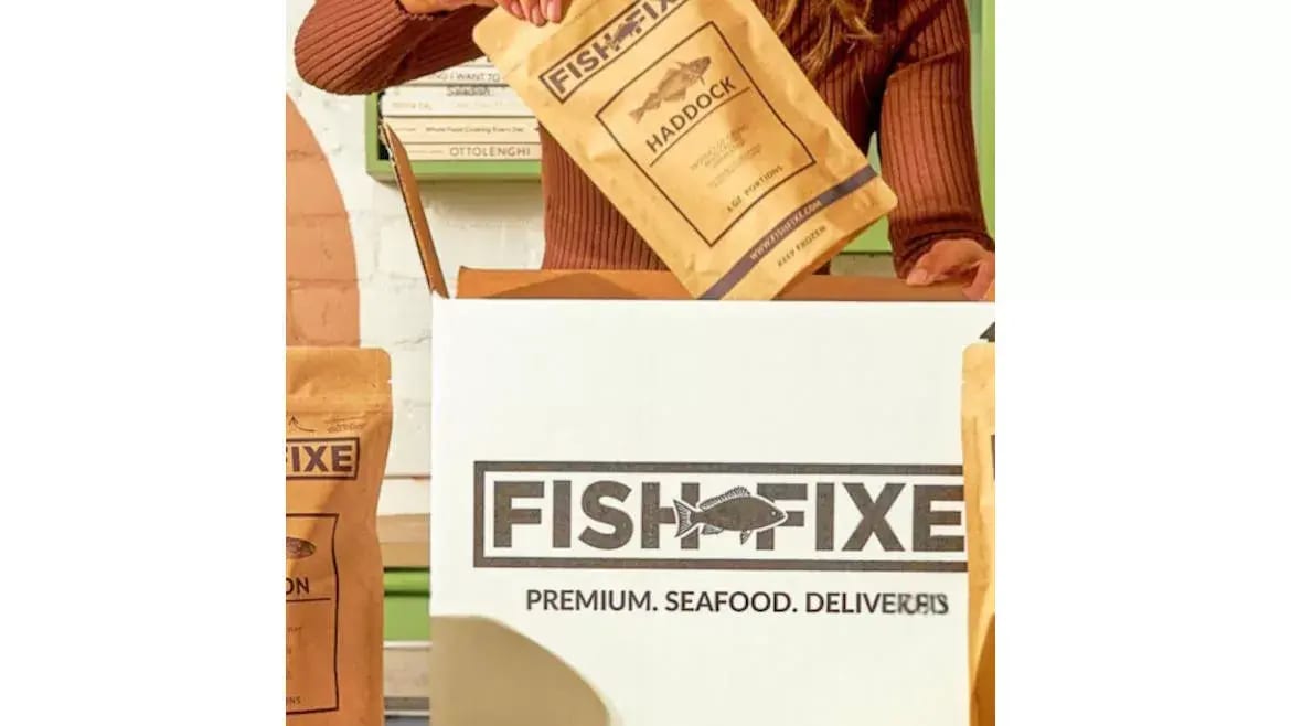 Hand placing a "Fish Fixe Haddock" seafood package into a branded delivery box.