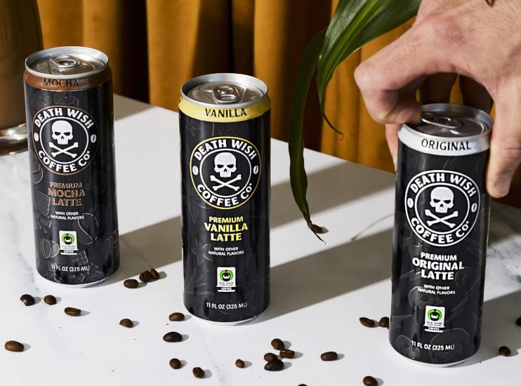 Three Death Wish Coffee Co. latte cans (Mocha, Vanilla, Original) with scattered coffee beans.