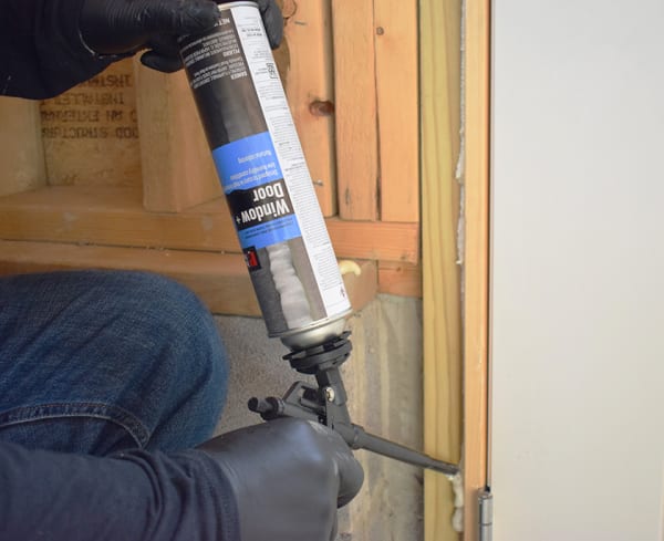 Person applying "Window + Door" insulating spray foam around a door frame.