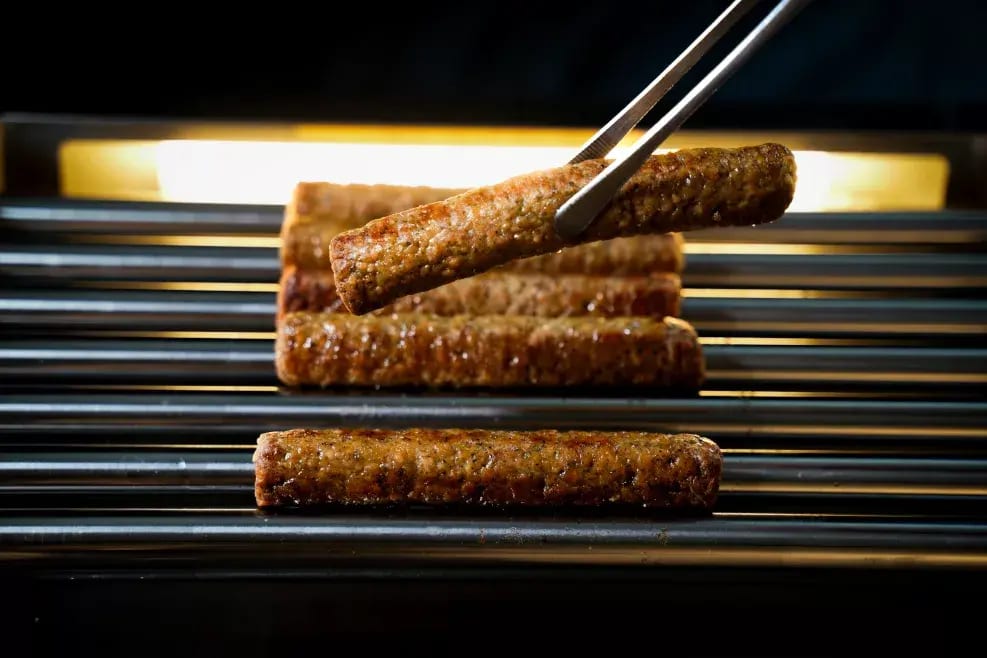 Grilled sausages on a hot grill, one lifted by tongs.